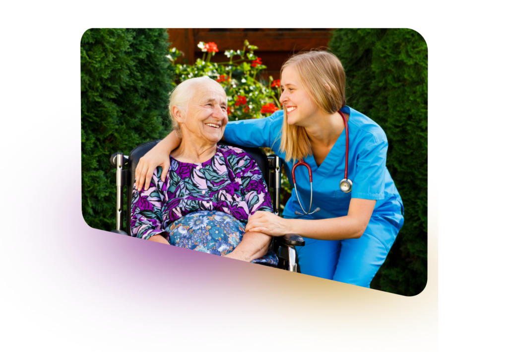 A young woman in a blue uniform and stethoscope smiles down at an elderly woman in a wheelchair, both laughing together outdoors. The image conveys a sense of care and connection.